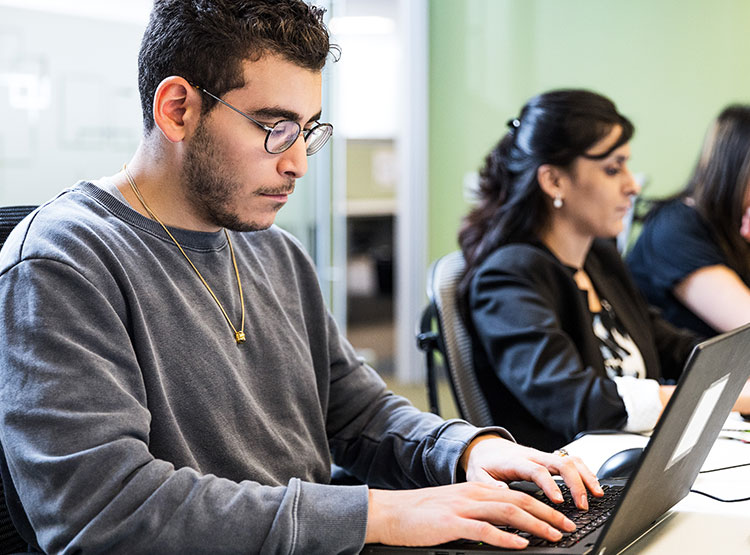 Three people work on laptop computers at a communal table.